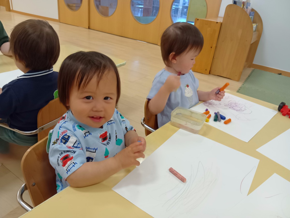 室内では、乳児たちが椅子に座って画用紙になぐり書きをしている。