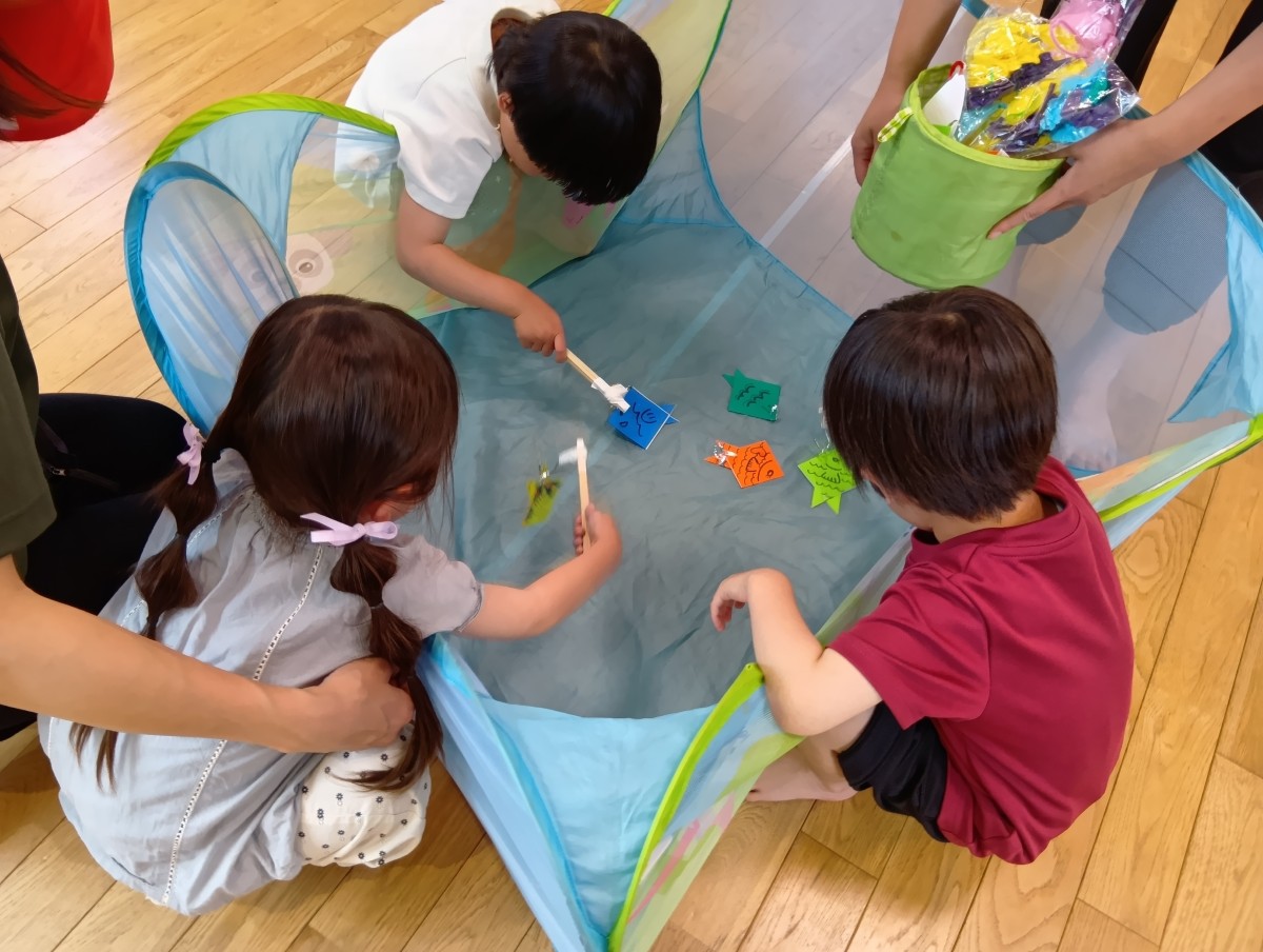 子どもたちが釣り竿のフックを折り紙の魚に引っ掛けようとしている。