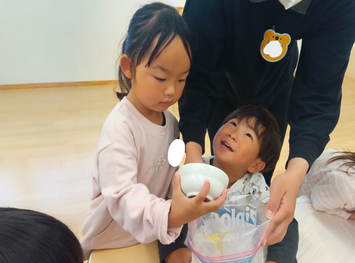 一人の子どもがジッパー付きポリ袋を広げ、もう一人の子どもが袋の口に向かって茶碗を傾けている。