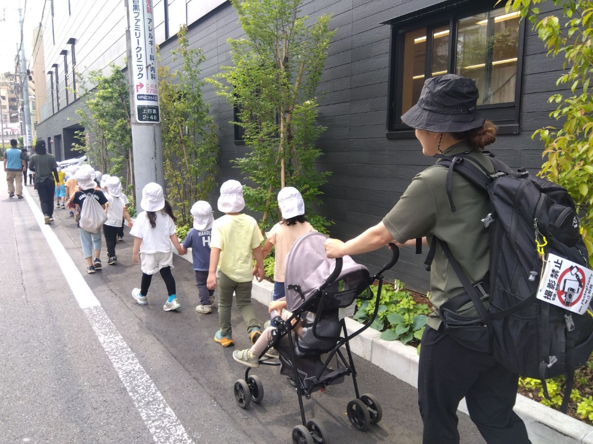 子どもたちは手をつないで歩道を歩き、4人の大人は列の先頭から最後尾まで等間隔に子どもの傍を歩いている