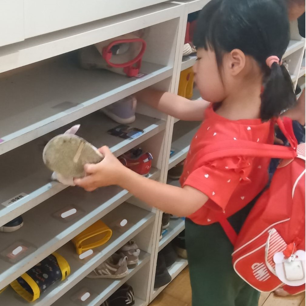 靴箱では、一人の子どもが自分の写真を見て靴をしまおうとしている。