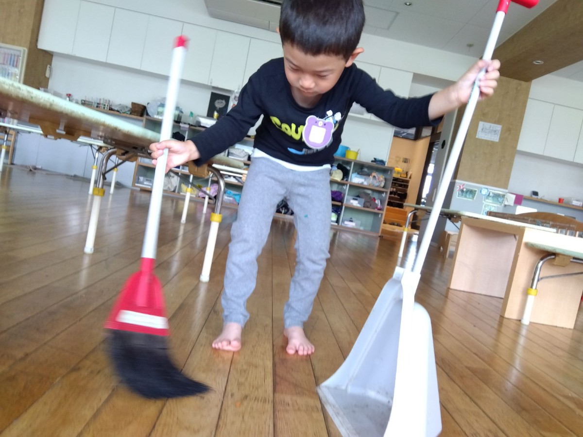 一人の子どもが箒と塵取りを手に持ち、かがんでゴミを掃いている。