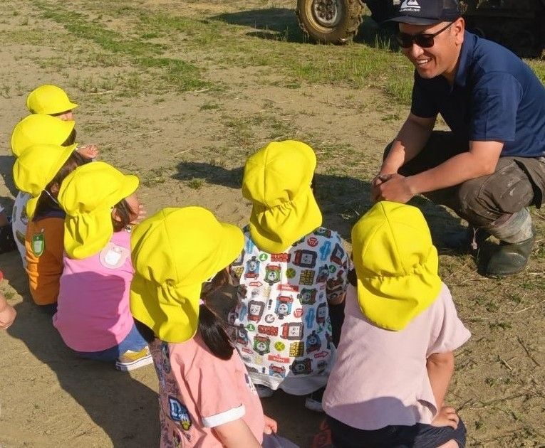 サングラスをかけた男の人が、座っている子どもたちに笑顔で話しかけている。