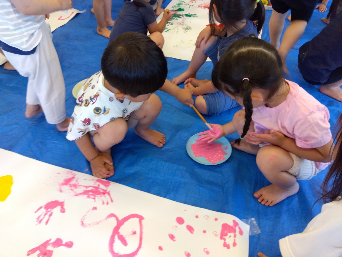 一人の子どもが筆を使って友達の掌に絵の具をつけている