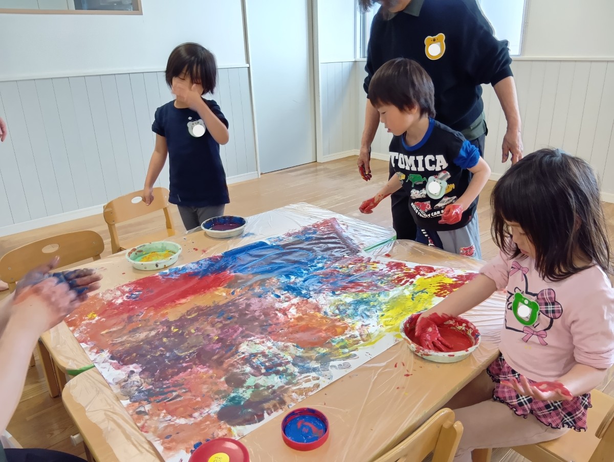 子どもたちは大きな模造紙に手や指を使って絵具を広げている