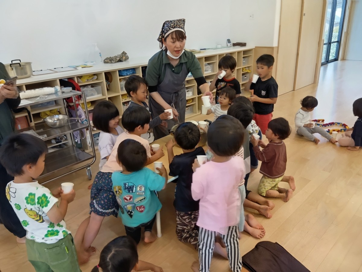 エプロンをつけた大人が子どもたちが手に持っている紙コップに出汁を入れている。