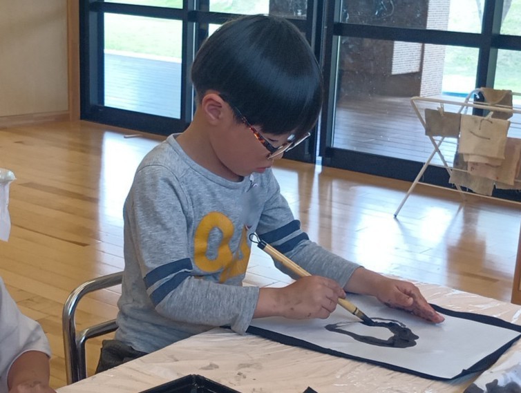 一人の子どもが背筋を伸ばして筆を使って半紙に墨で丸を描いている