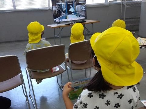 室内では、子どもたちが椅子に座って映像を見ている