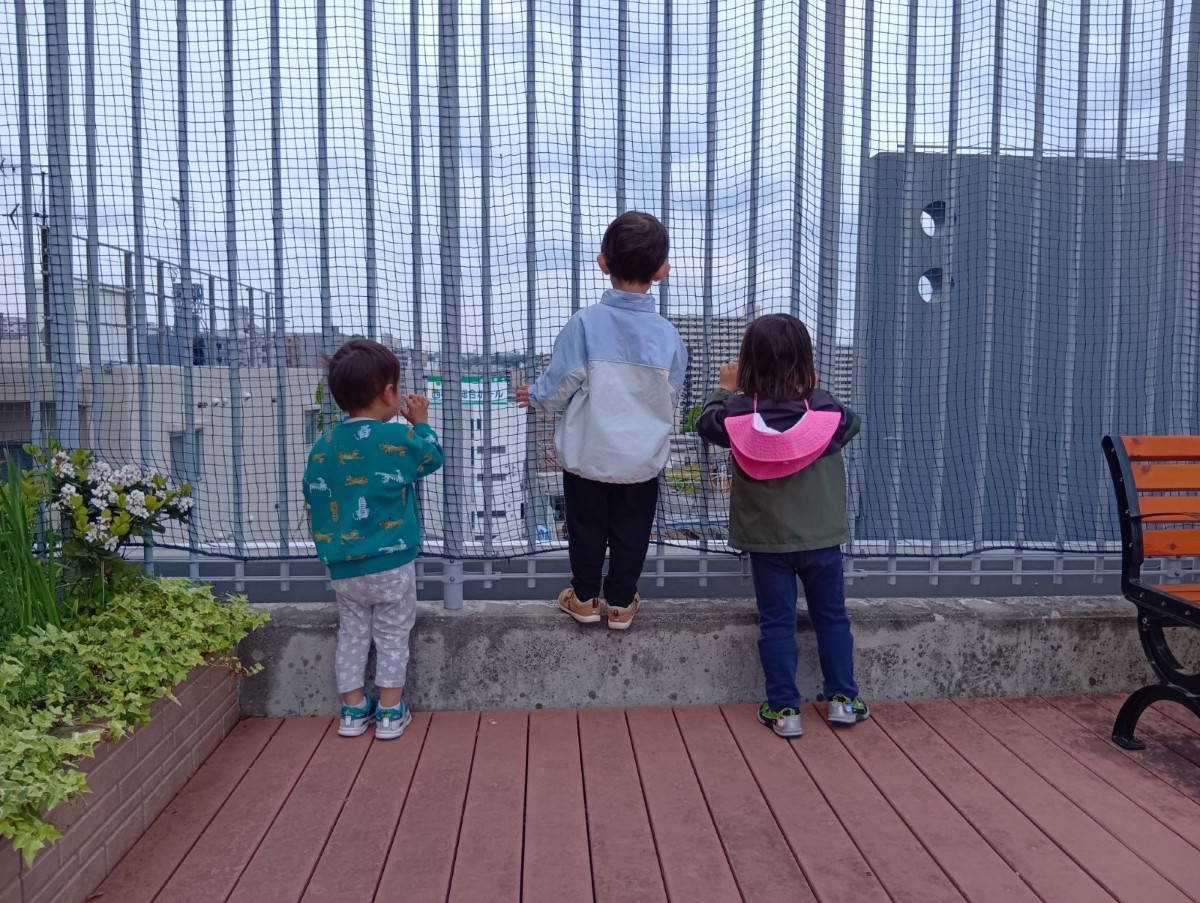 テラスの端に並んで立つ3人の子どもたちの後ろ姿