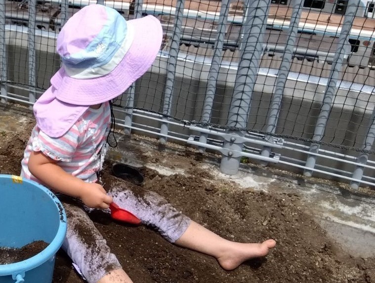 シャベルを持った裸足の子どもが土をかけて土に座っている