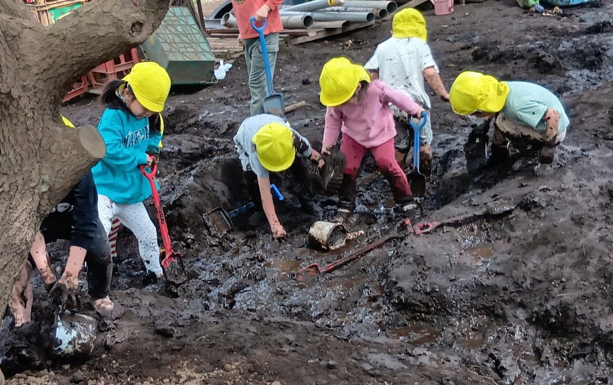 シャベルやバケツを持った子どもたちが、泥だらけになりながら泥を掘ってくぼみを作っている