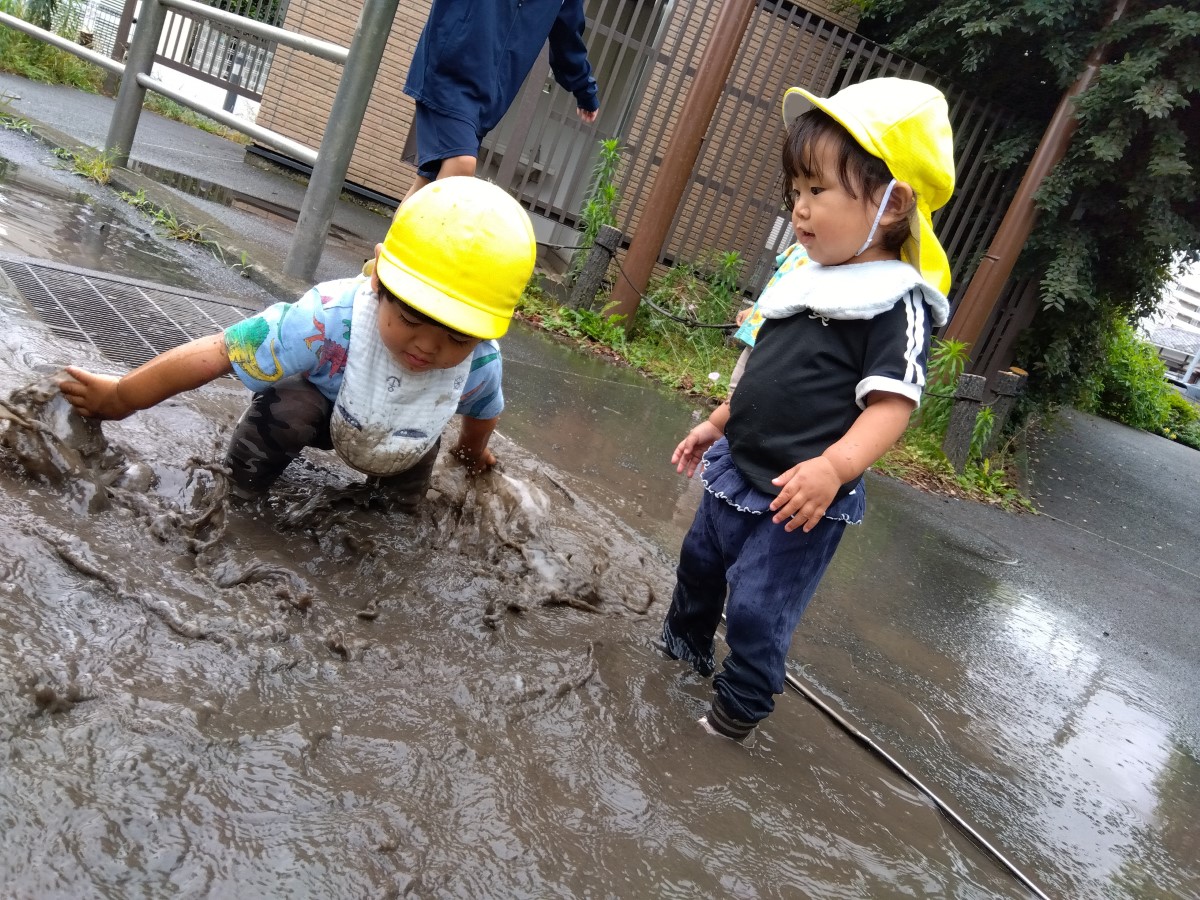 雨水溜まりでは、水を手でかき混ぜる子、水の中で混ざる泥水の様子を見る子がいる。