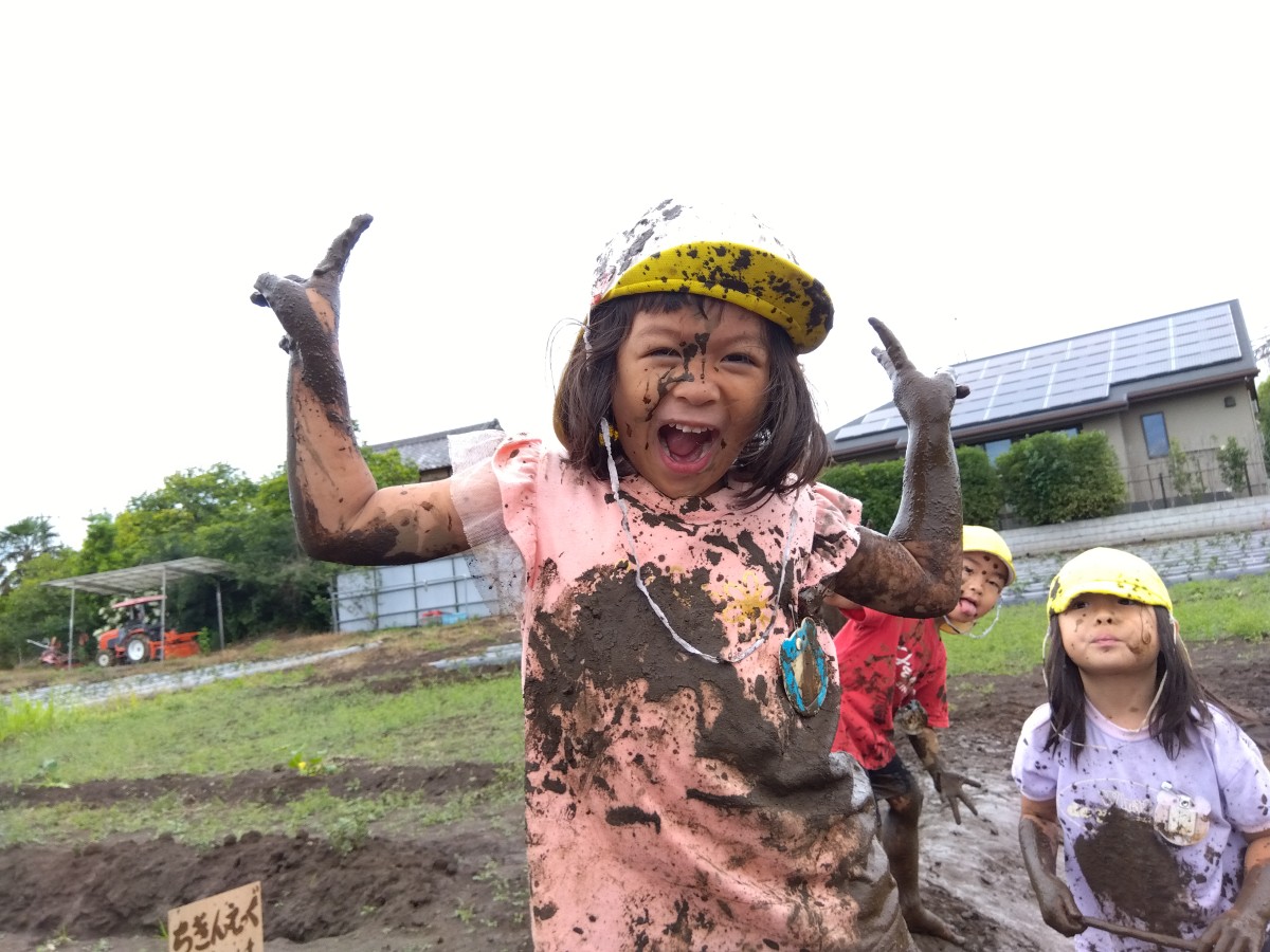泥だらけになった子どもがピースサインをして笑顔でこちらを見ている