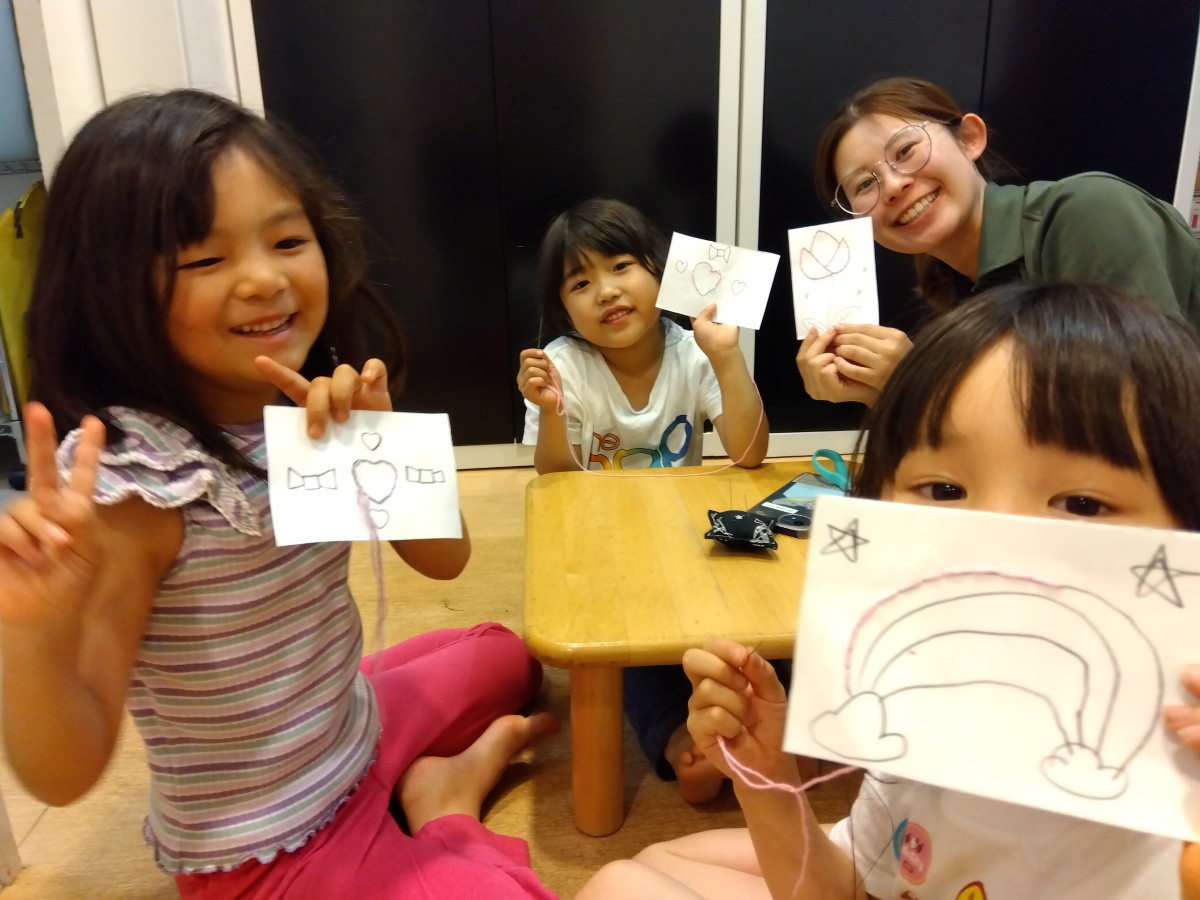 ハートや虹が描かれた線の上を太い糸で縫っている子どもたちと大人