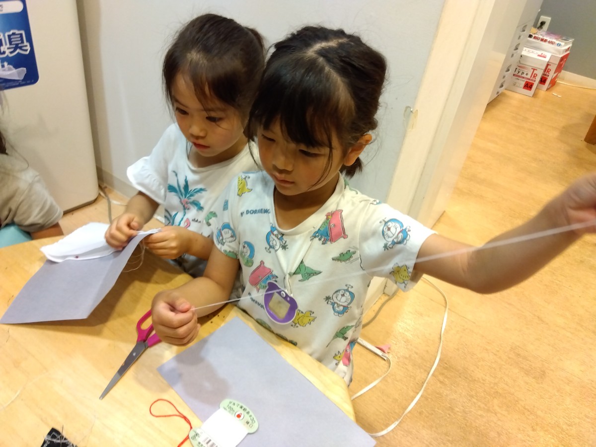 一人の子どもが針に糸を通した後、糸を縒ろうとしている