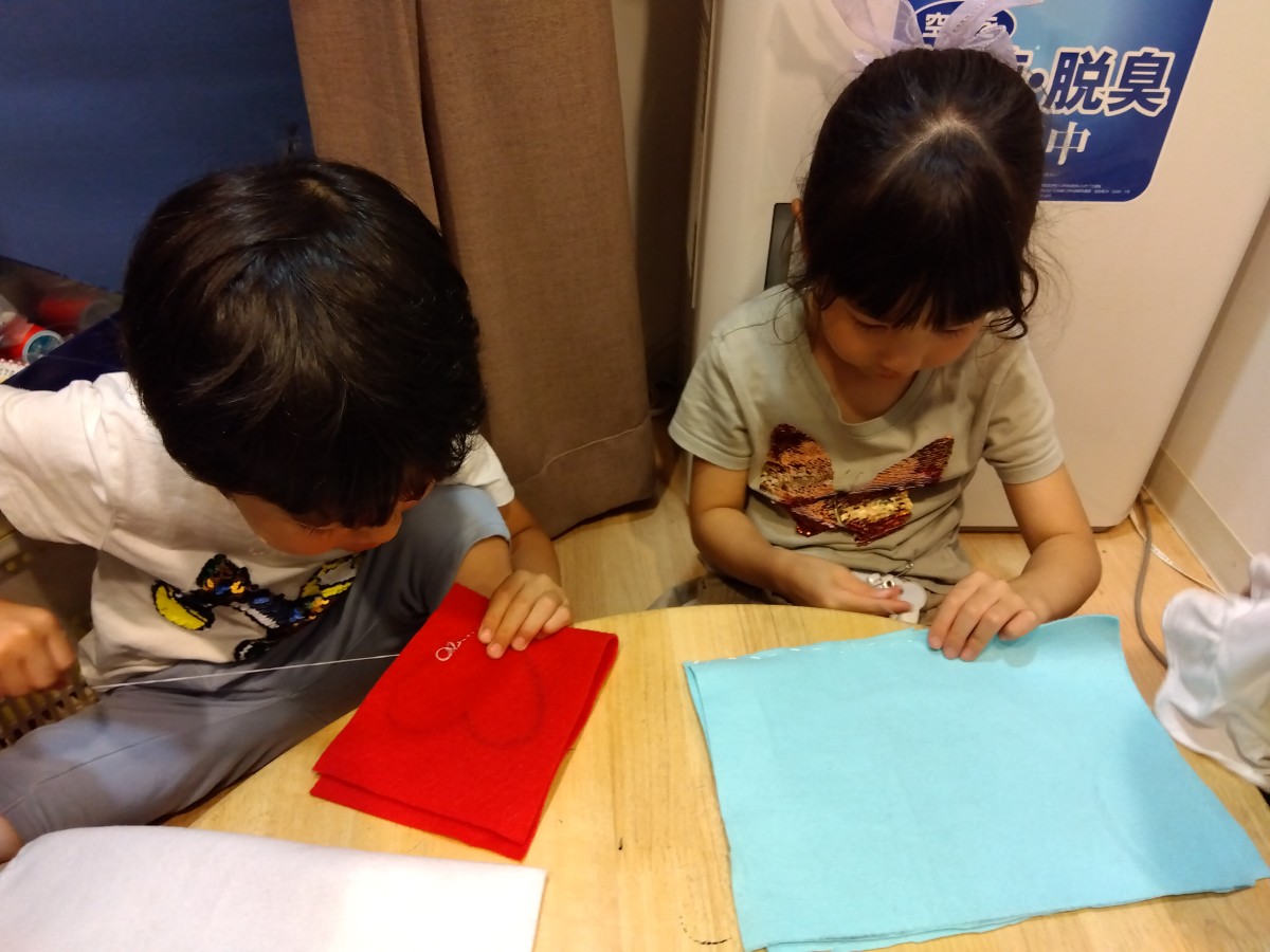 二人の子どもがフェルトを2枚に重ねて線の上や重なったフェルトの端を糸で縫っている