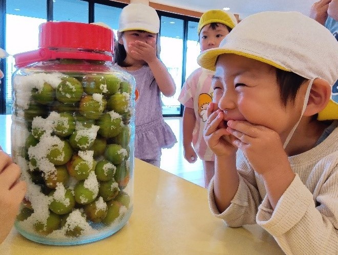 机の上に梅と塩が入った瓶が置かれており、子どもたちは手を口に当てて笑っている