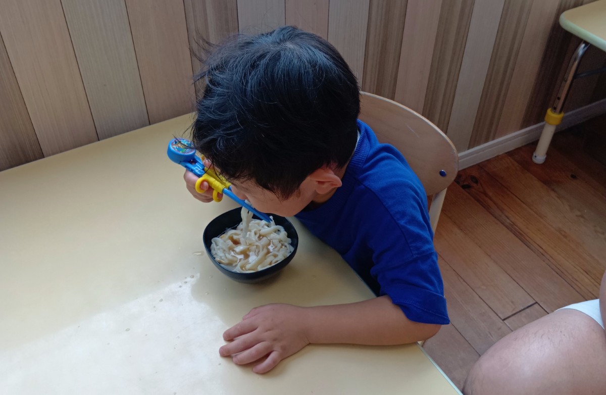 一人の子どもが補助箸を使って作ったうどんを食べている