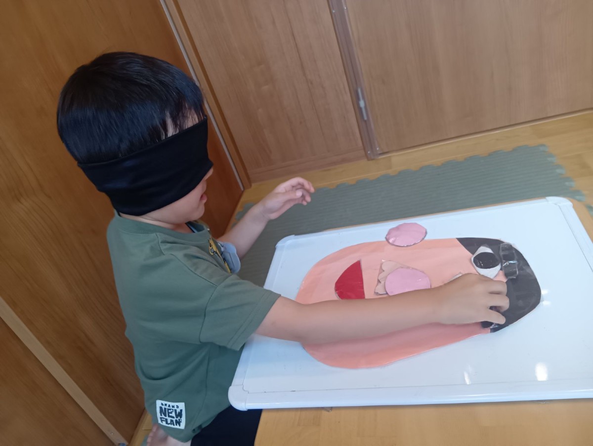 目隠しをした一人の子どもが、画用紙でかたどられた顔の上に目のパーツを置いている