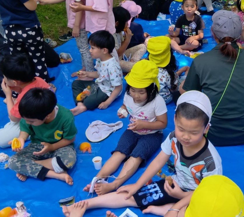 シートの上で子どもたちと大人が弁当を食べている