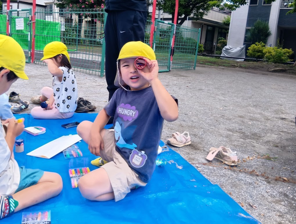 公園では、シートの上で子どもたちがペンやカラーフィルムを使って望遠鏡を作っている