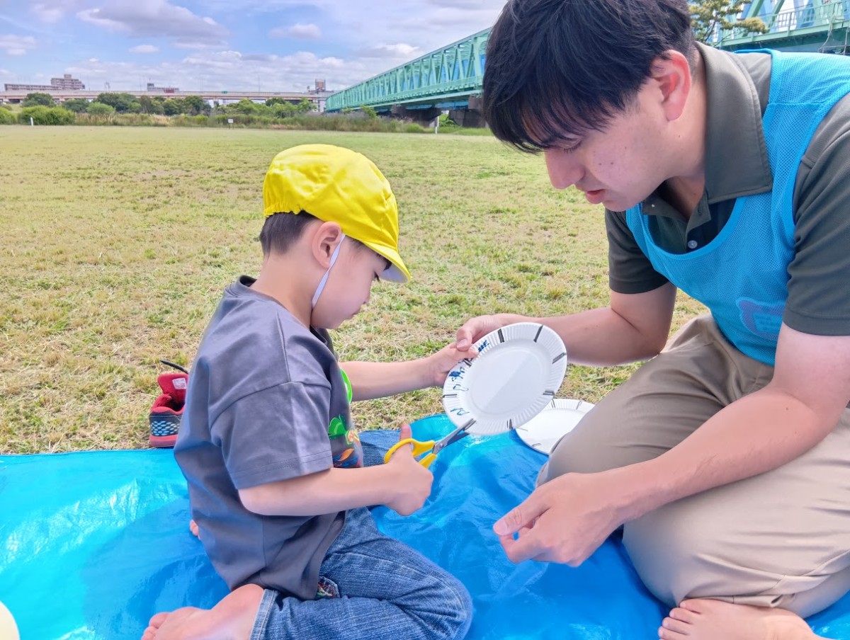 一人の子どもが印線が書かれた紙皿にハサミをあてて切ろうとしており、一人の大人は子どものハサミを持っていない反対の手を支えている