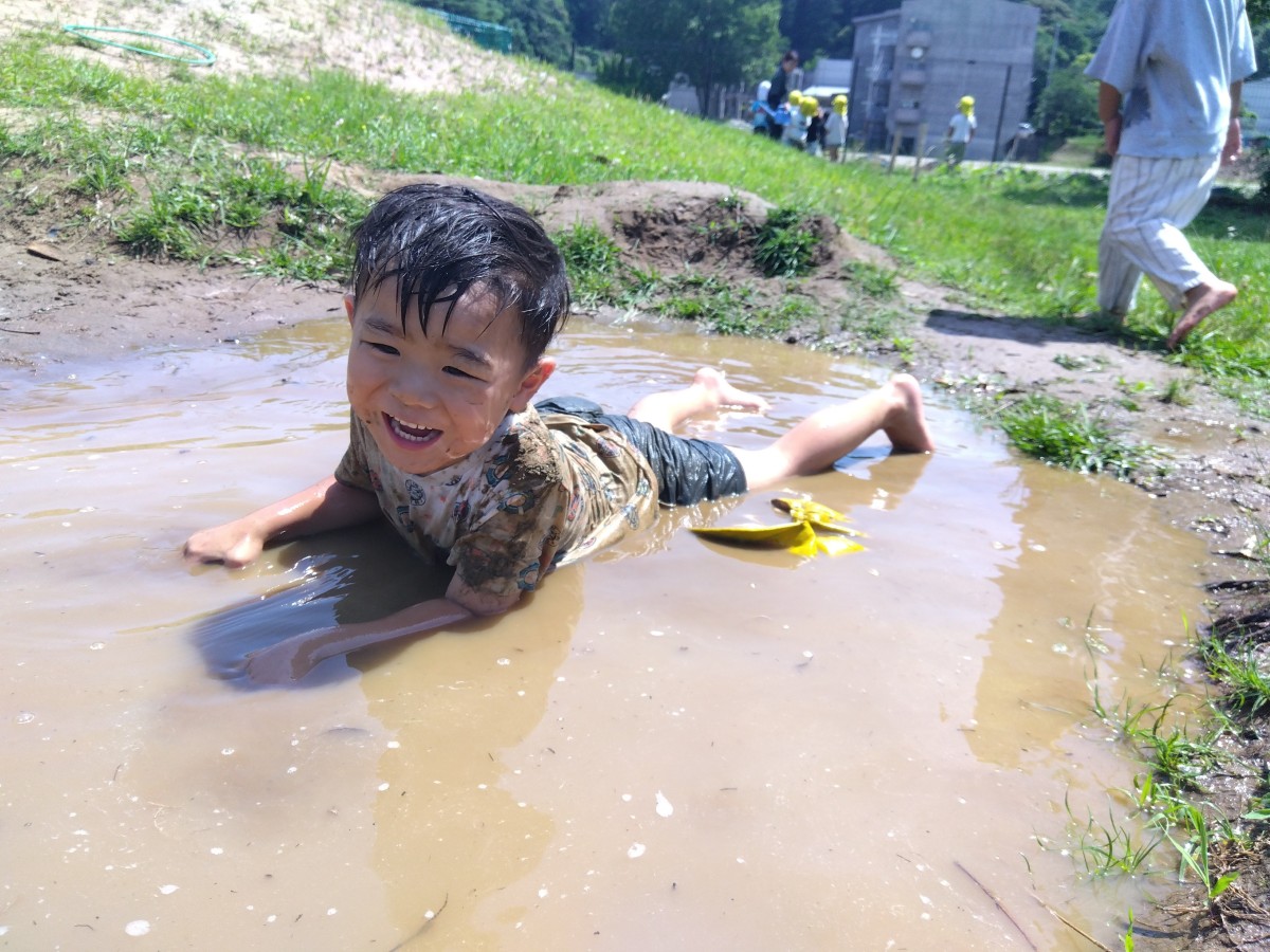 一人の子どもが泥の水またりに横になって笑っている