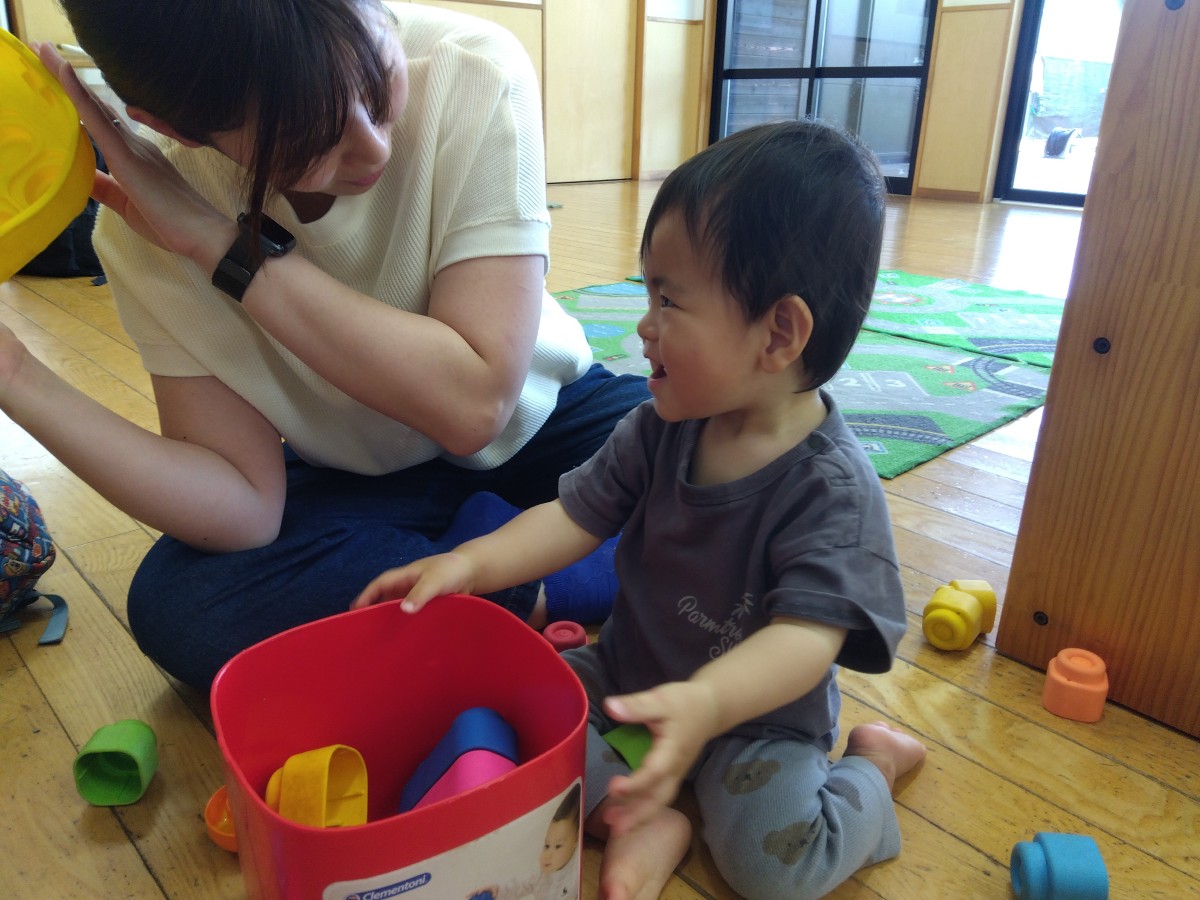 ソフトブロックで遊ぶ子どもと大人が視線を交わすと、子どもが笑顔をみせている