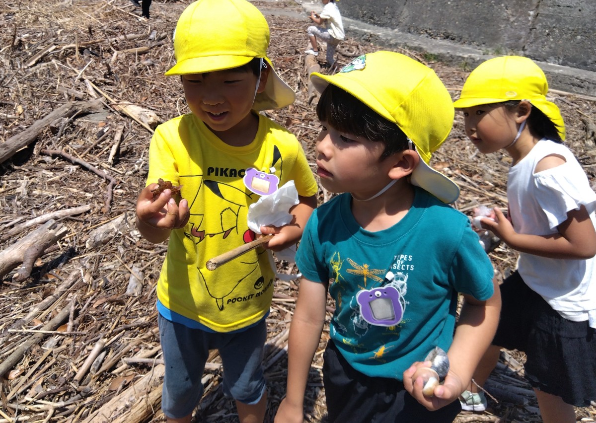 一人の子どもが笑顔でカニを片手で持ち、それを貝殻を手にもった隣にいた子が見ている