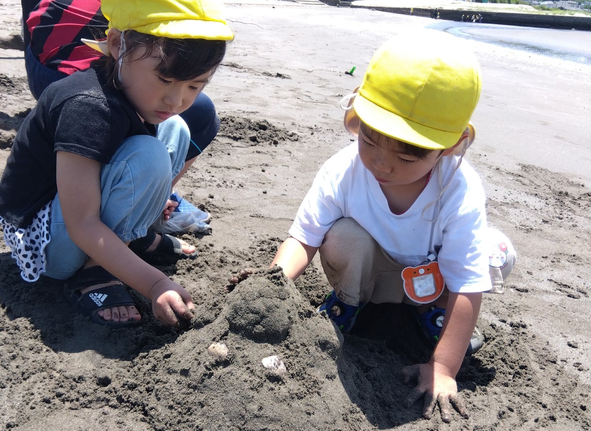 二人の子どもは貝殻を外側に飾りつけて砂山を作っている
