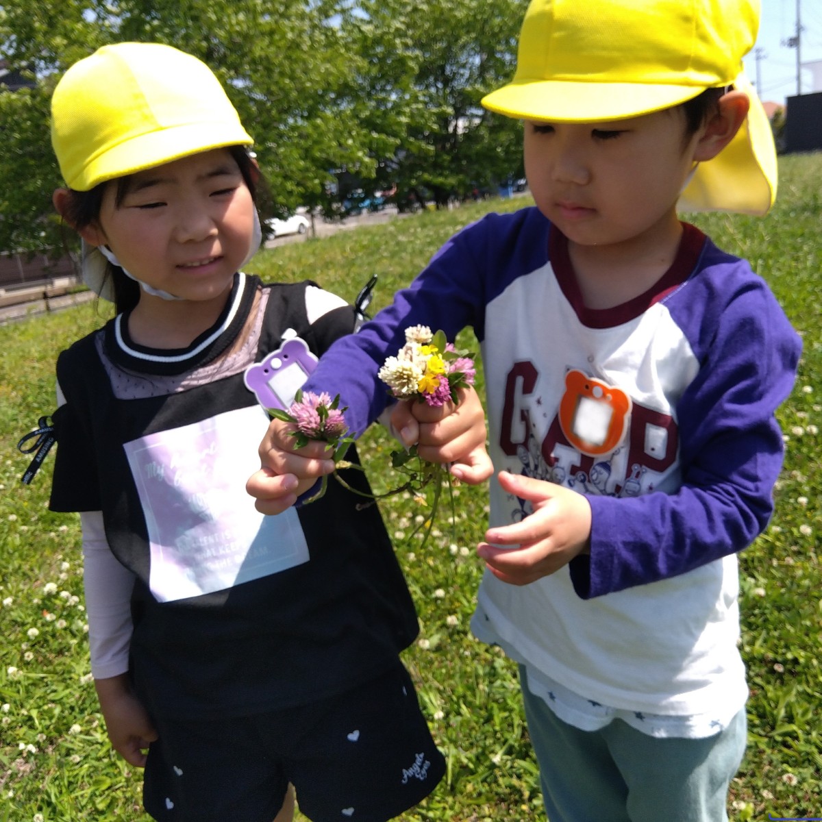 二人の子どもが花摘みで摘んだ花束を見せ合っている