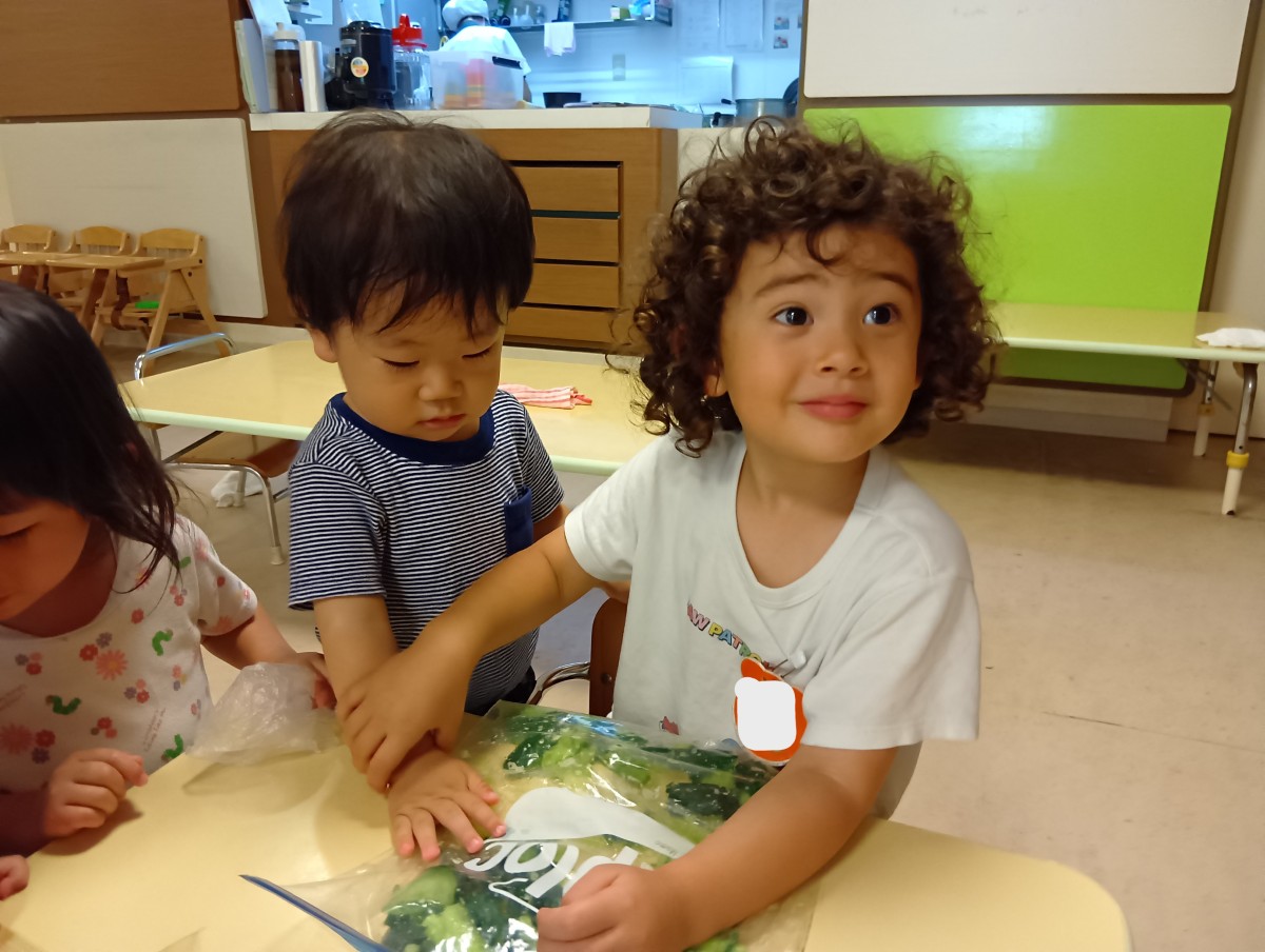 一人の子どもが年下児の手を取り、ジッパー付きポリ袋に入ったきゅうりを触れるように促している