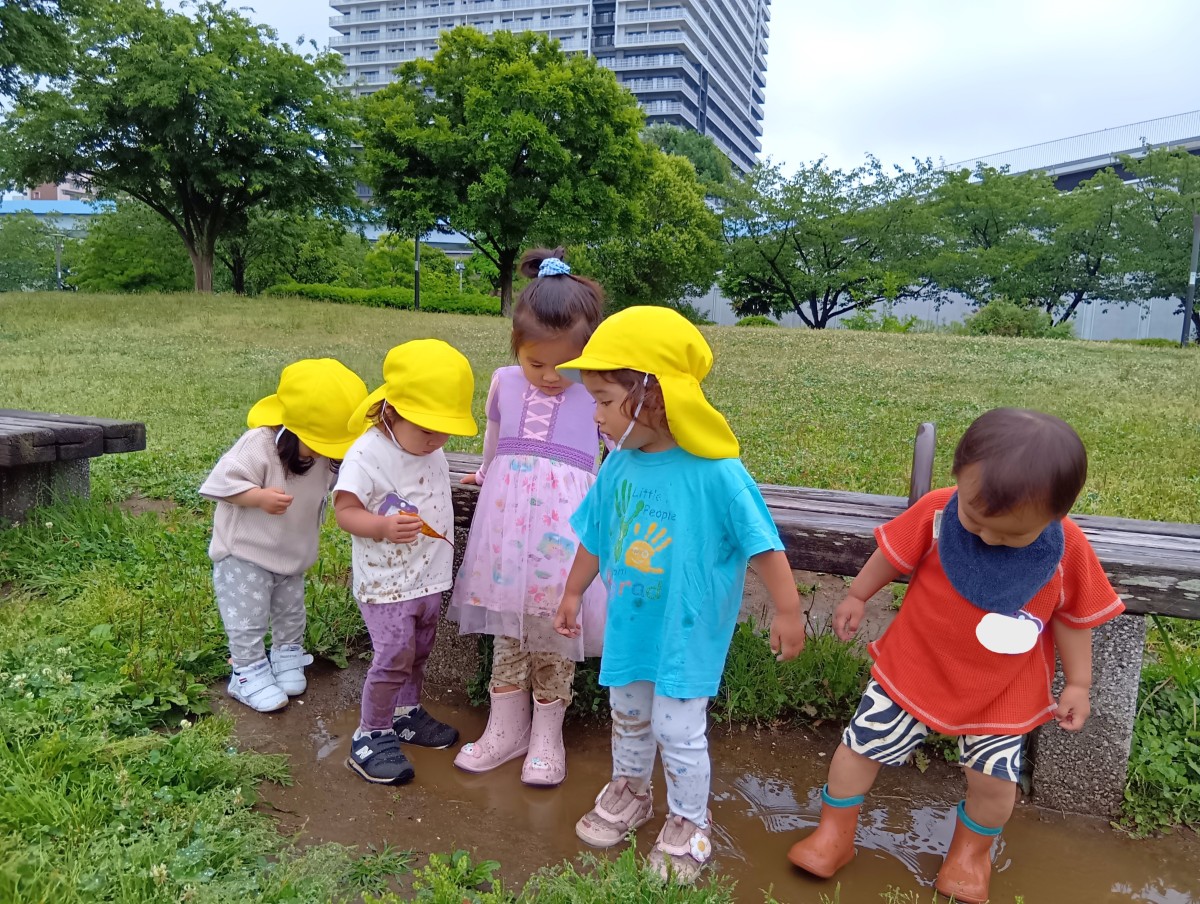 長靴や運動靴を履いた子どもたちが水たまりの中で足元を見ながら足を動かしている