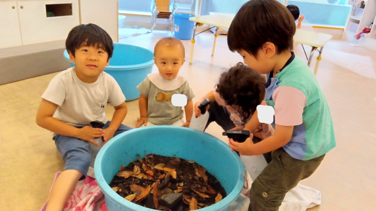 子どもたちは、落ち葉や石がたくさん入った大きなバケツを囲み、霧吹きで水を吹きかけている