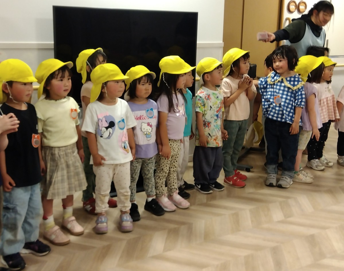 施設内で、一人の大人と顔を赤くした子どもたちが一列に並んで前に立っている