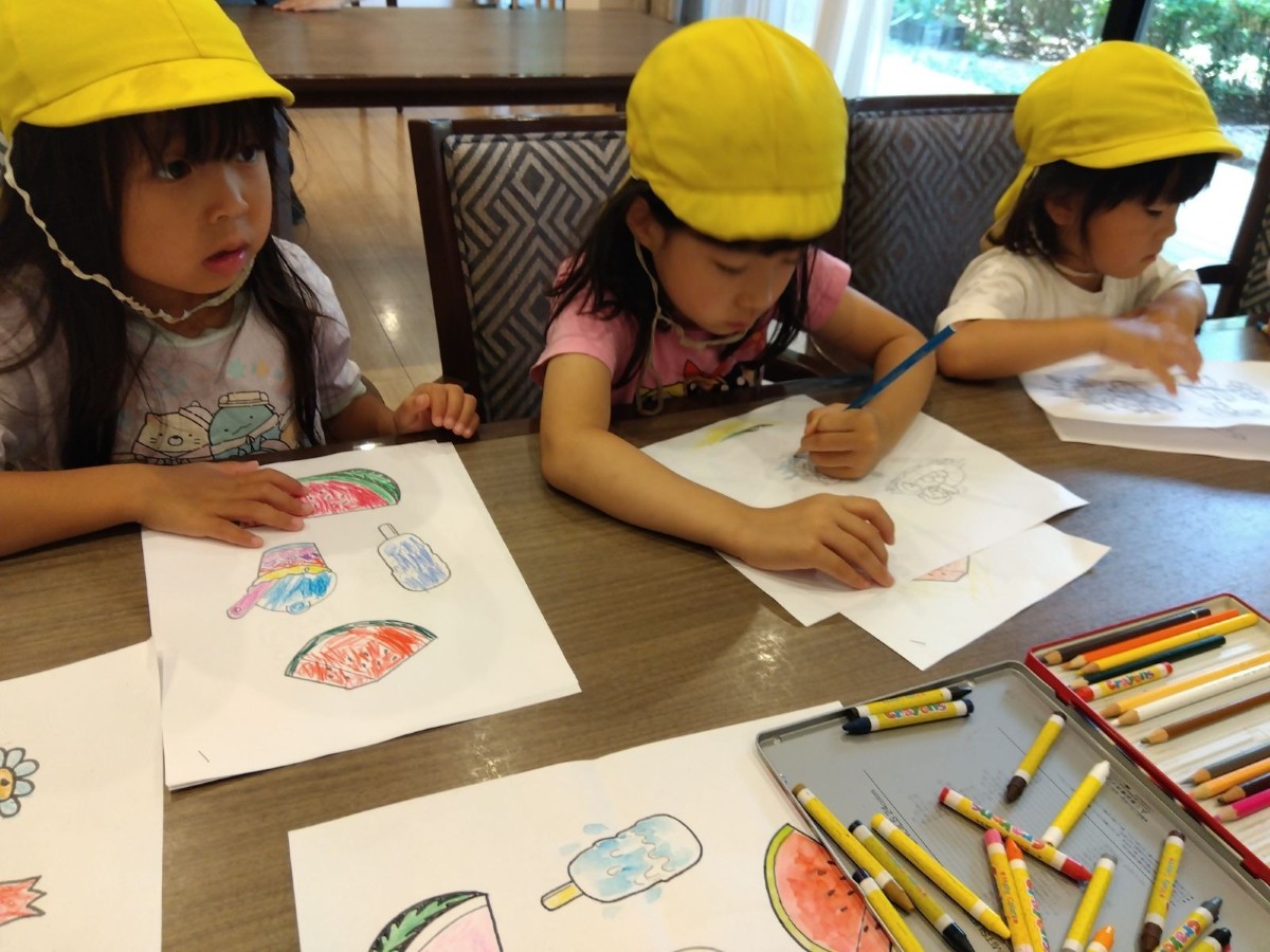 ３人の子どもが椅子に座り塗り絵をしている