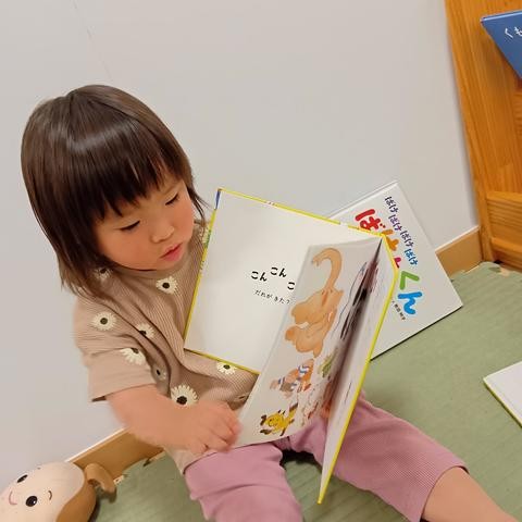 絵本棚の前で、一人の子どもが絵本を横に向けて開いている