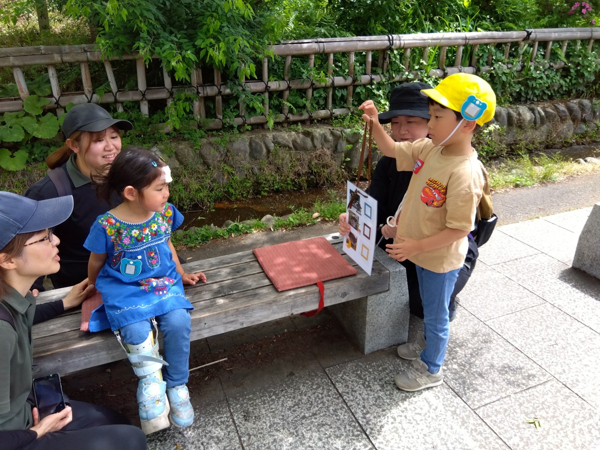 一人の子どもが散歩マップを手に持って立ち、もう一人の友達に散歩マップを見せている