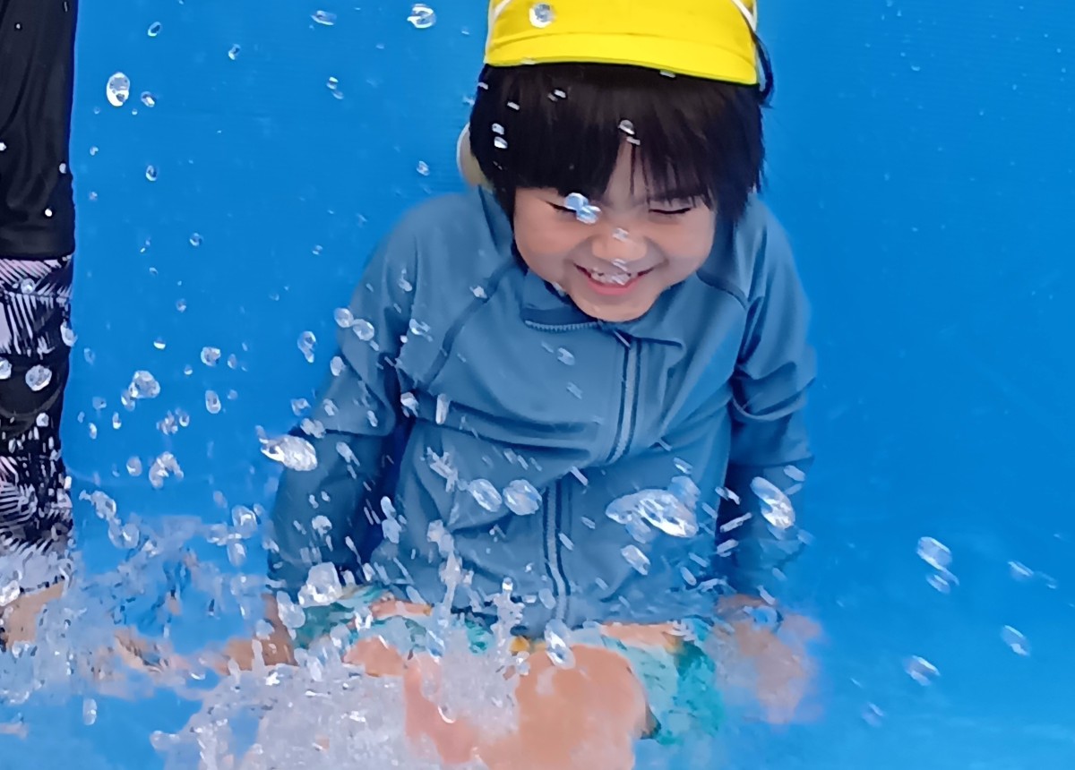 水遊びで、一人の子どもが水しぶきを感じて笑っている