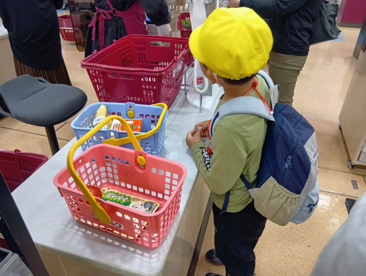一人の子どもが、スーパーマーケットのレジに買い物かごを置いて順番を待っている