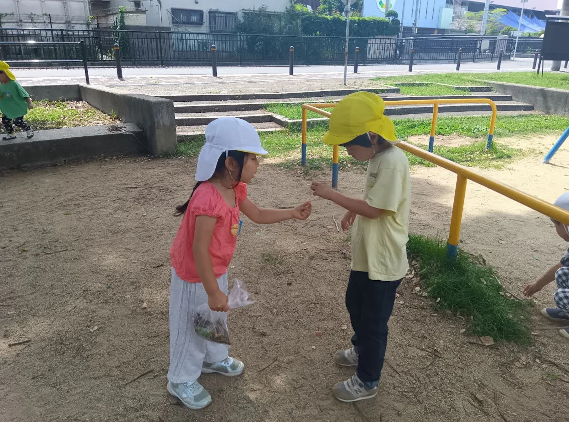 公園では、一人の子どもが自分で見つけたものを友達に渡している