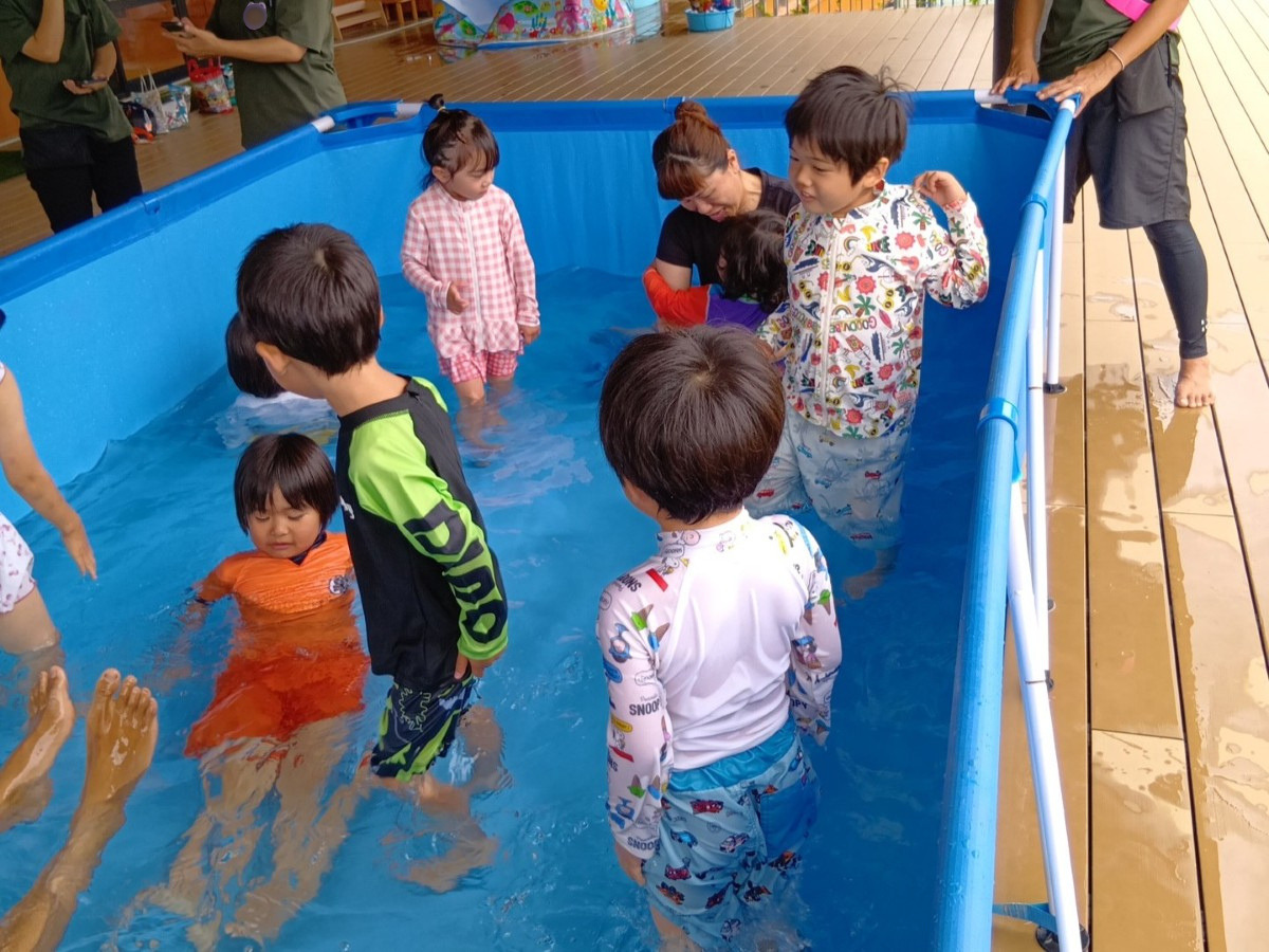プールの中では、足を伸ばして水に浸かる子、大人に抱き着いて水の中に入る子、水の中を歩いている子などがいる