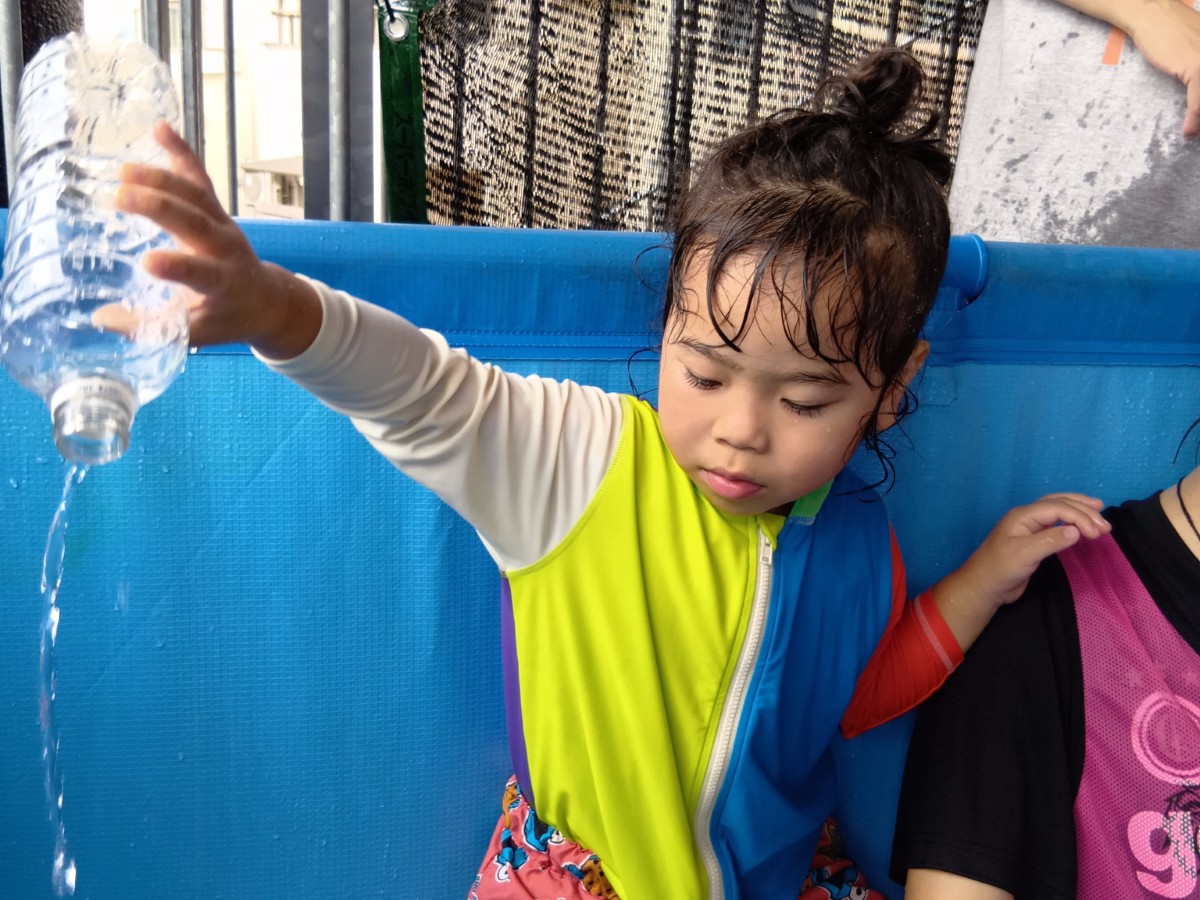 一人の子どもがペットボトルの水をプールの中に注ぎ、水の動きを見ている