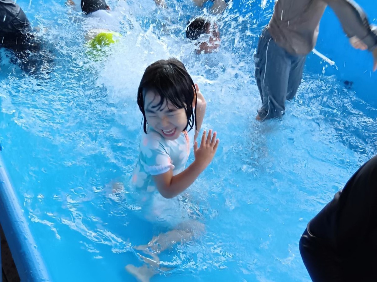 一人の子どもがプールの中で水しぶきを浴びて笑顔を見せている