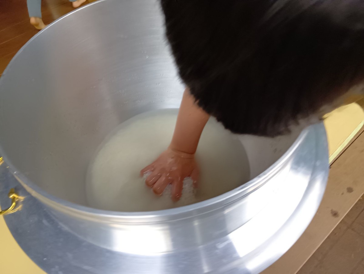 一人の子どもが米と水が入った釜の中に手を入れて水の量をみている