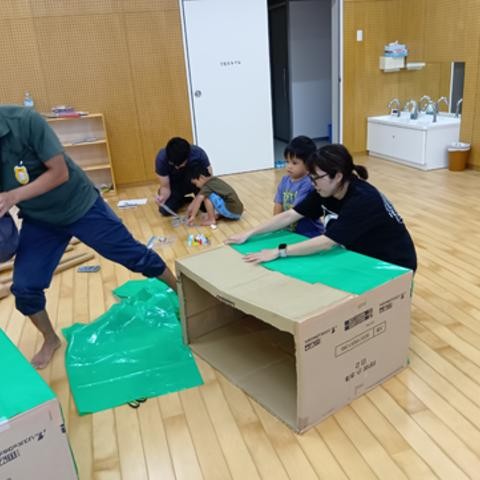 室内では、こどもたちと大人で段ボールに色付きポリ袋を押さえたり貼ったりして制作をしている