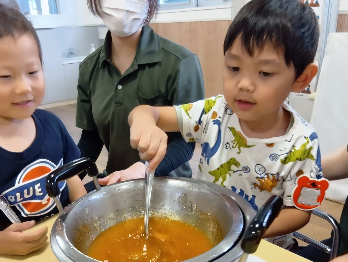 一人の子どもがスプーンを使ってジャムを混ぜており、隣でもう一人の子どもがその様子を見ている