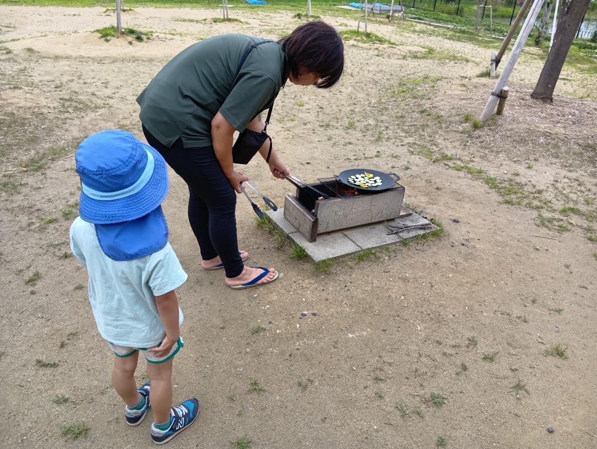 スタッフは焚き火でズッキーニを焼いており、一人の子どもが少し離れた場所でその様子を見ている