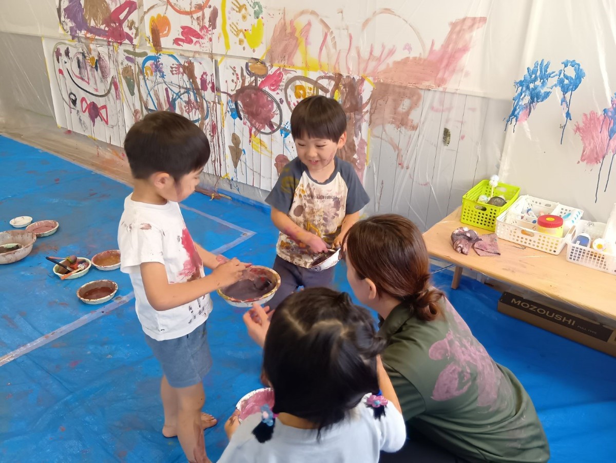 室内の壁はビニールシートと模造紙で覆われており、大人と子どもたちは絵の具を混ぜて壁や体に絵の具を付けている
