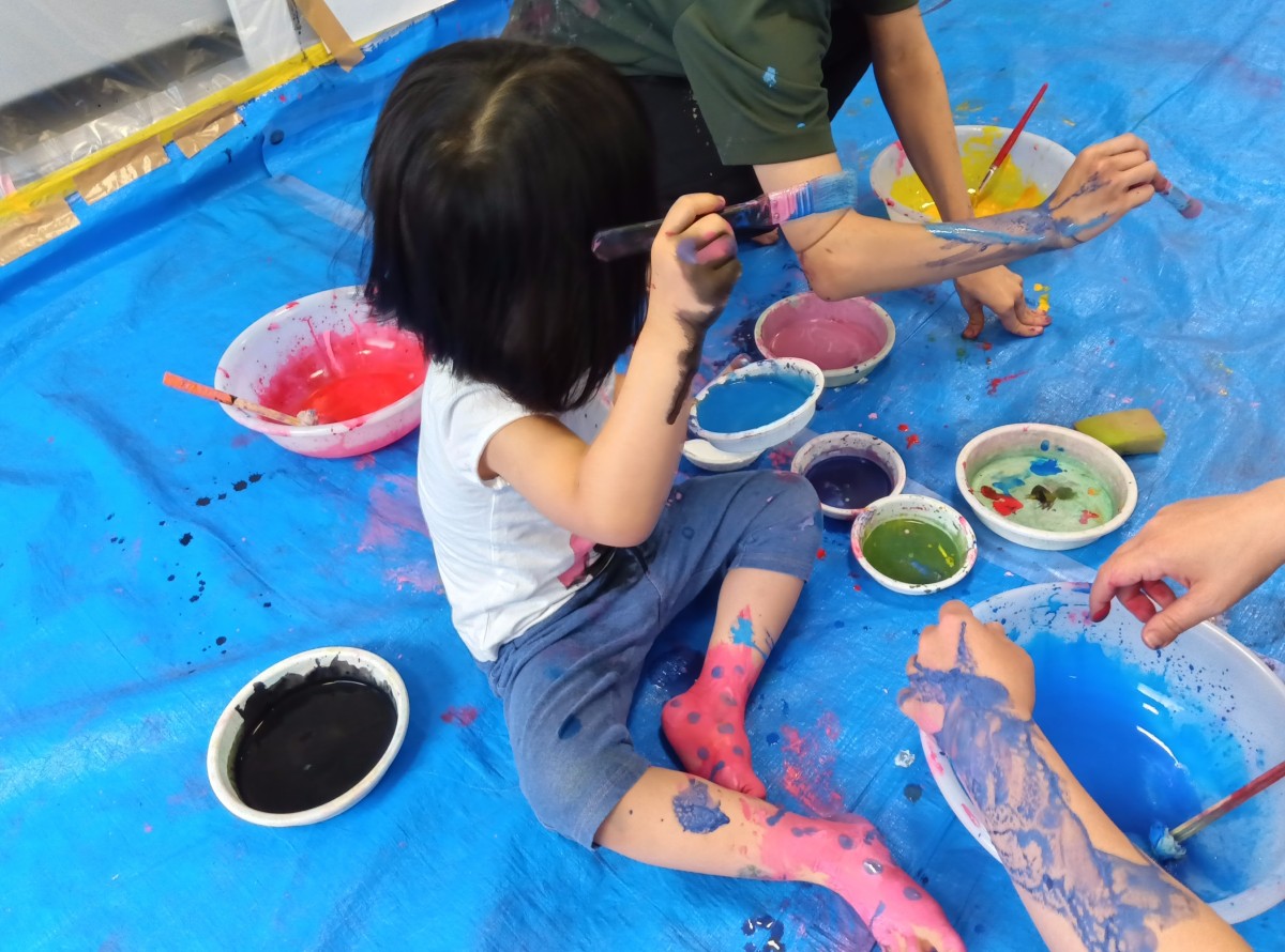 一人の子どもが自分の裸足に絵の具を使って水玉の靴下を描いている